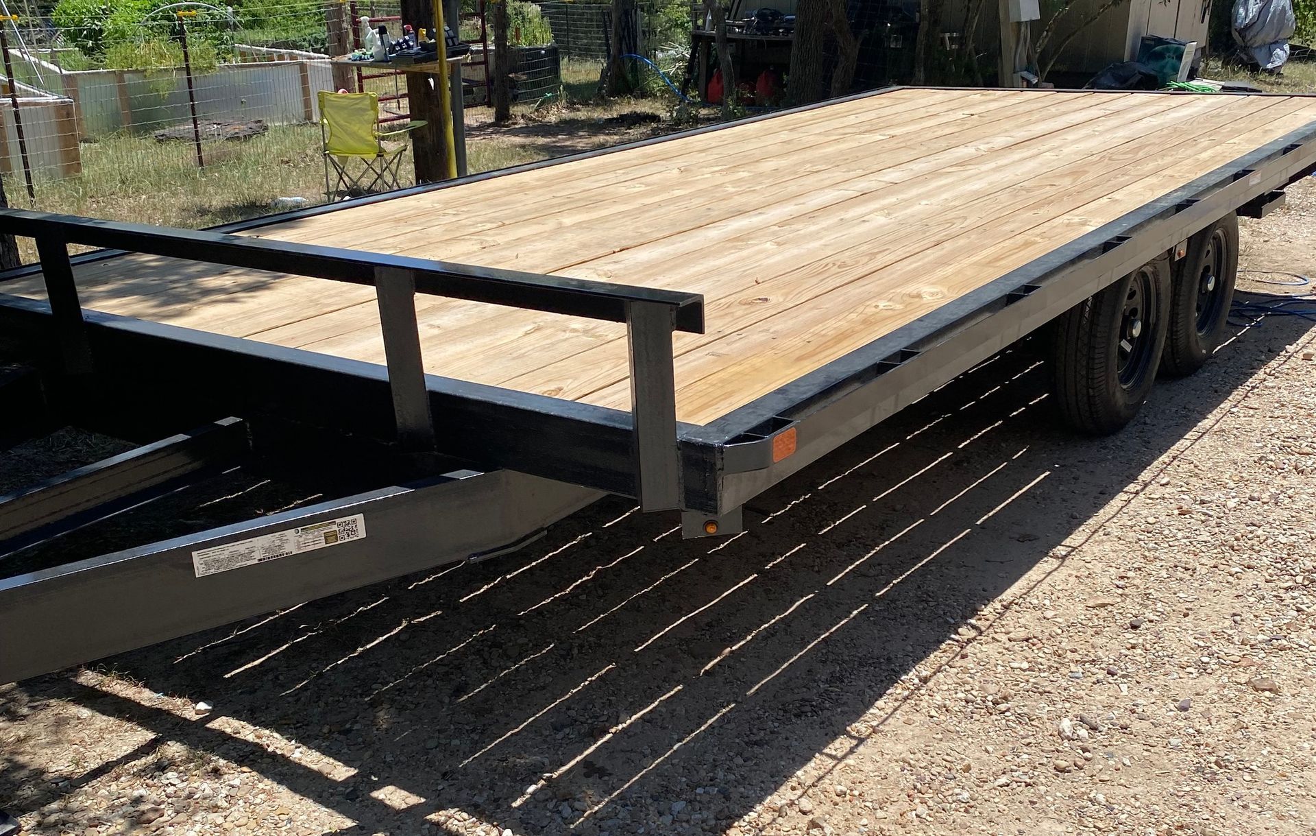 A trailer with a wooden deck is parked on gravel.