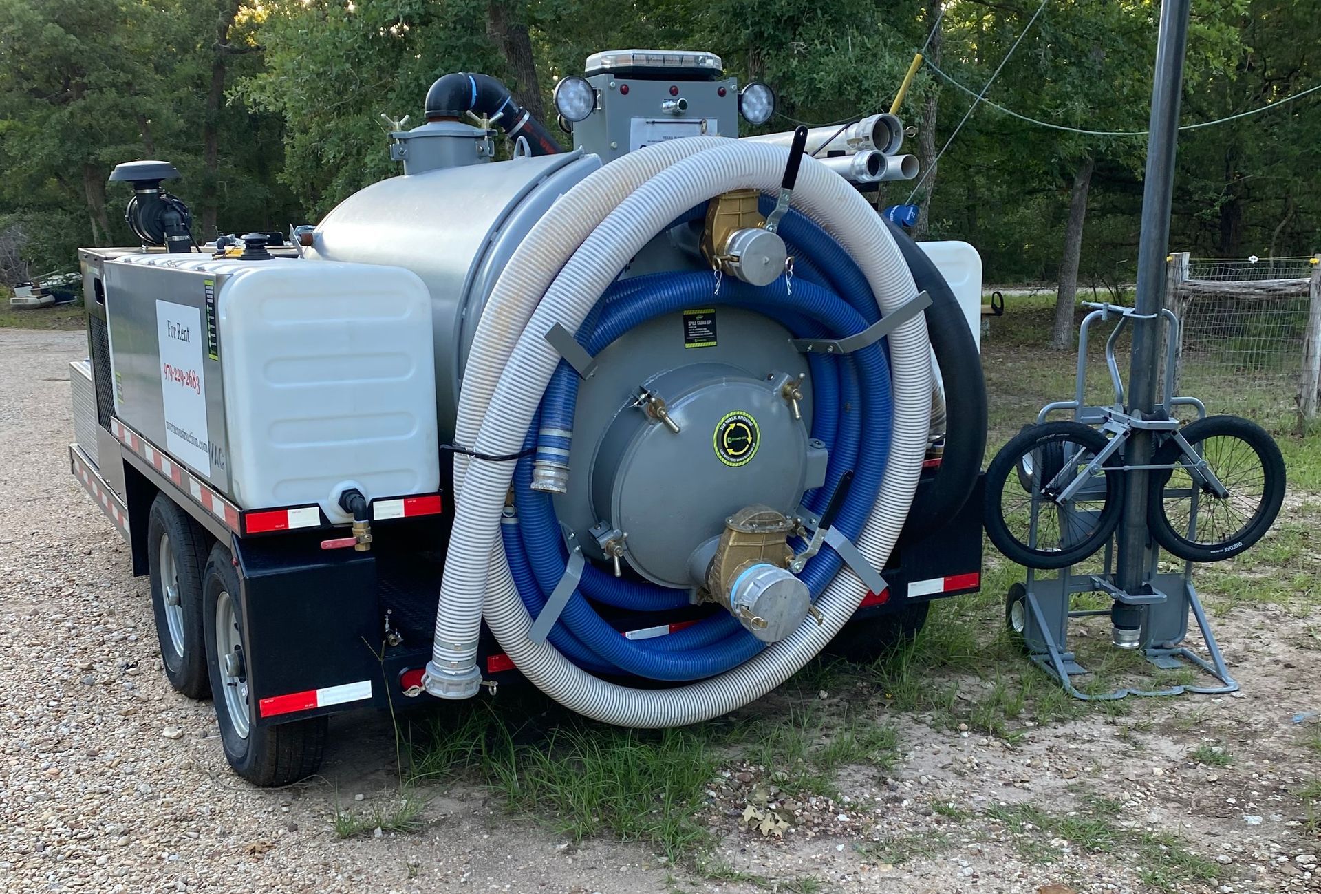 A vacuum truck with a large hose attached to it is parked on a gravel road.