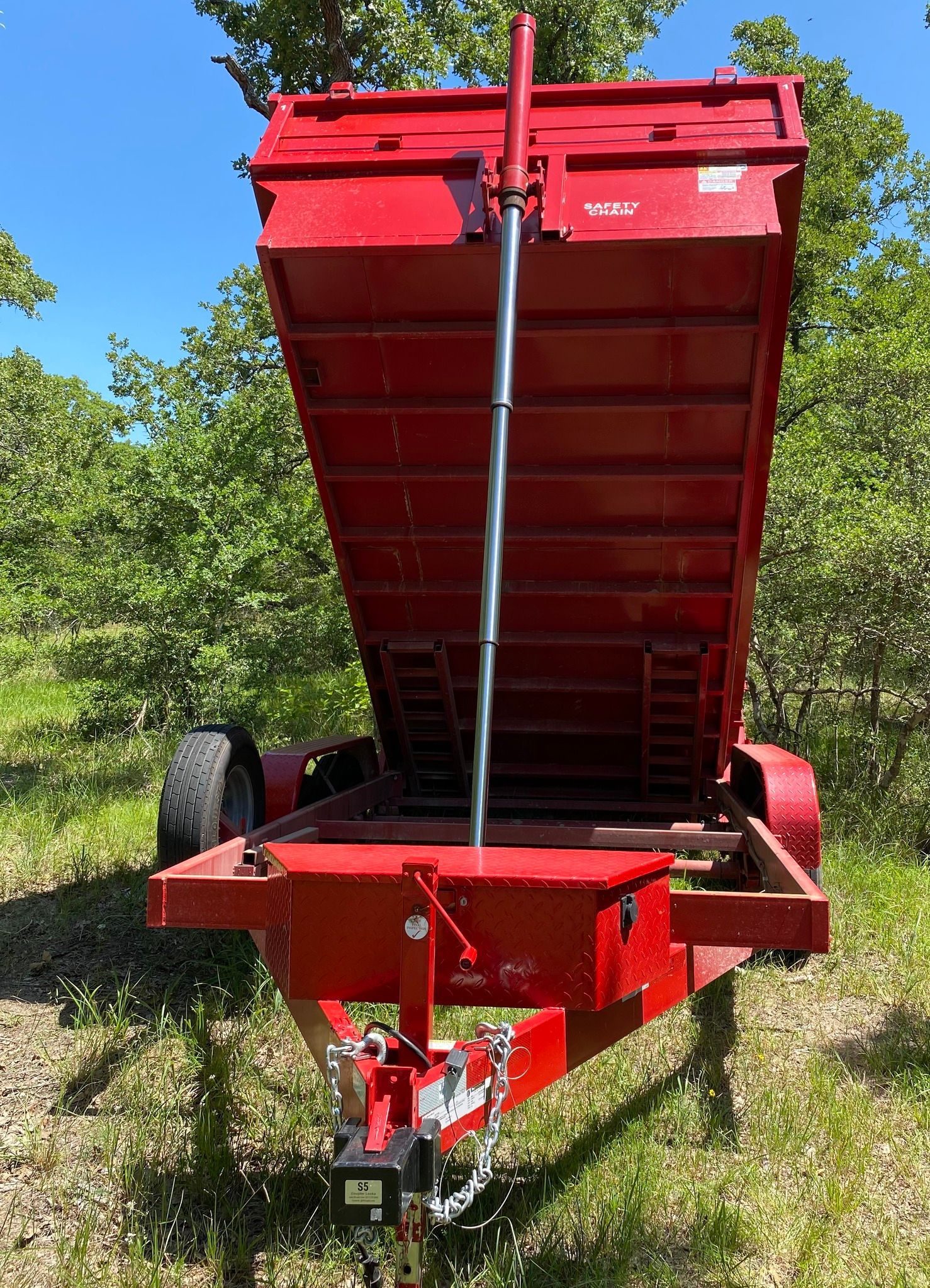 A red dump trailer is parked in a grassy field.