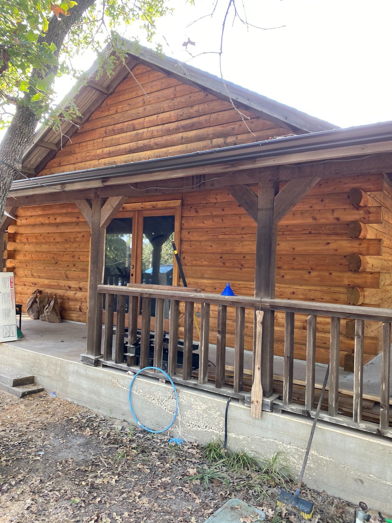 A log cabin with a porch and a hose on the side of it.