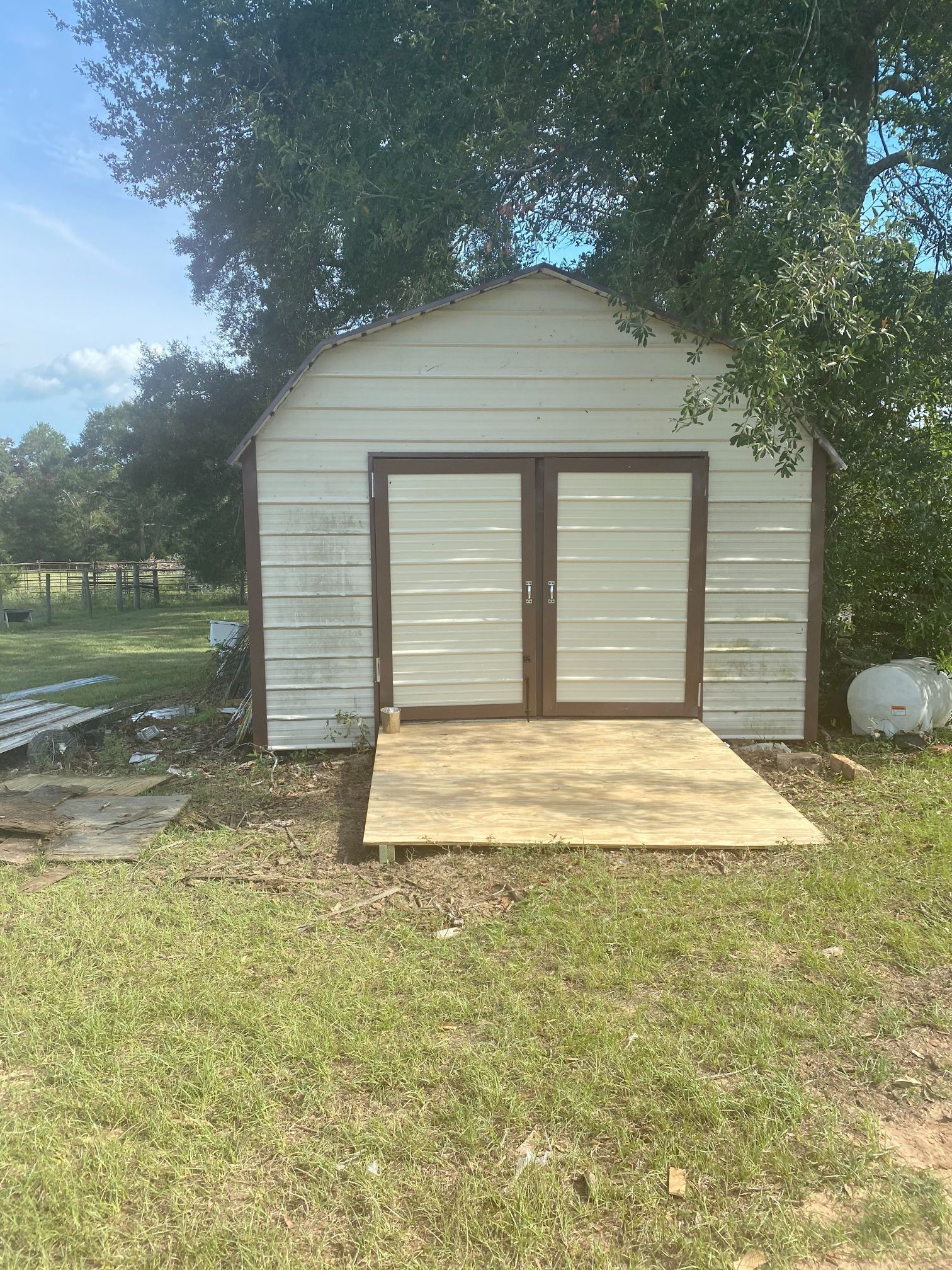 A white shed with a wooden deck is sitting in the middle of a grassy field.