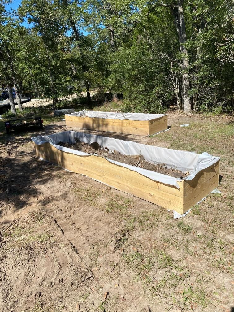 Three wooden raised beds are sitting on top of a dirt field.