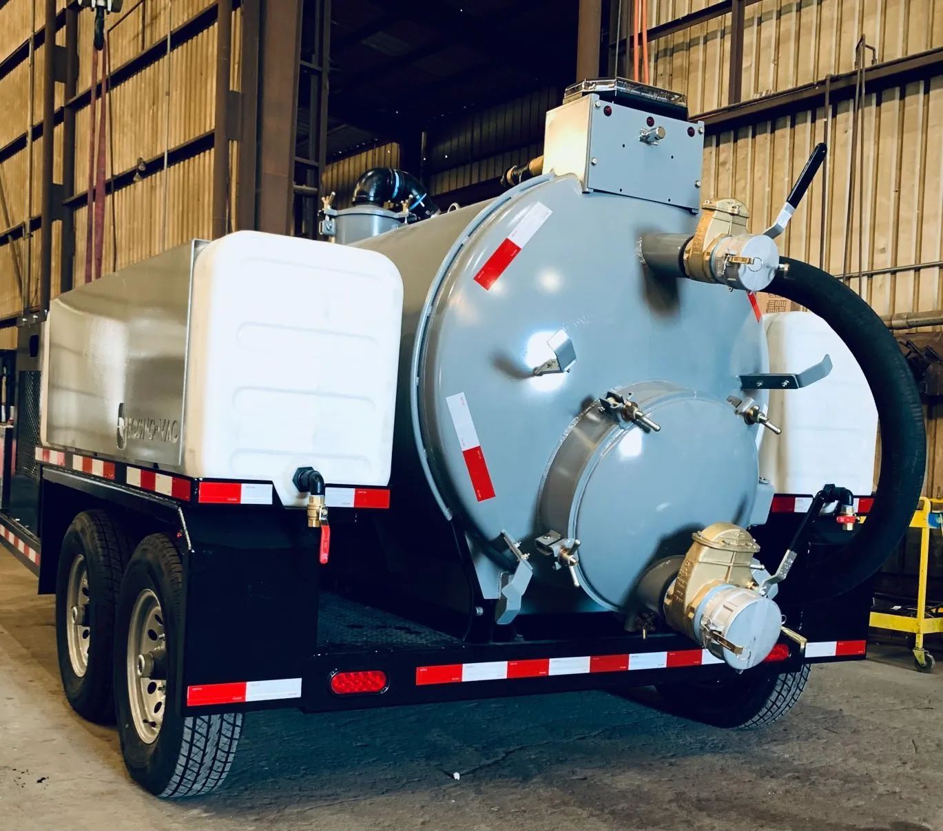 Industrial vacuum truck with large gray tank parked indoors in a warehouse garage.