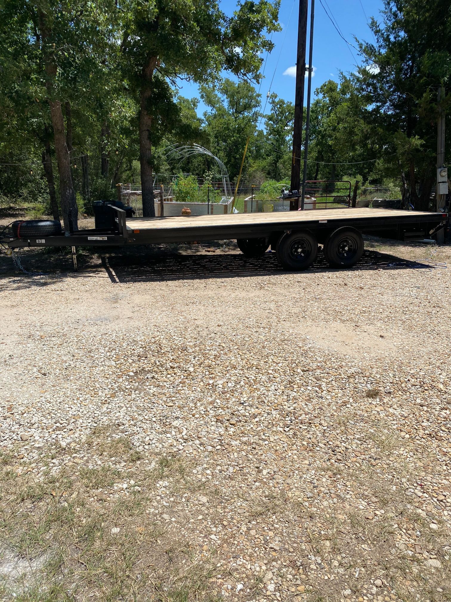 A flatbed trailer is parked in a gravel lot with trees in the background.