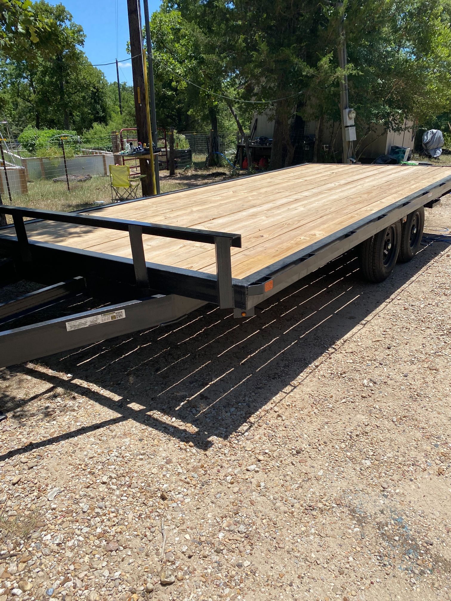 A flatbed trailer with a wooden deck is parked in a gravel lot.