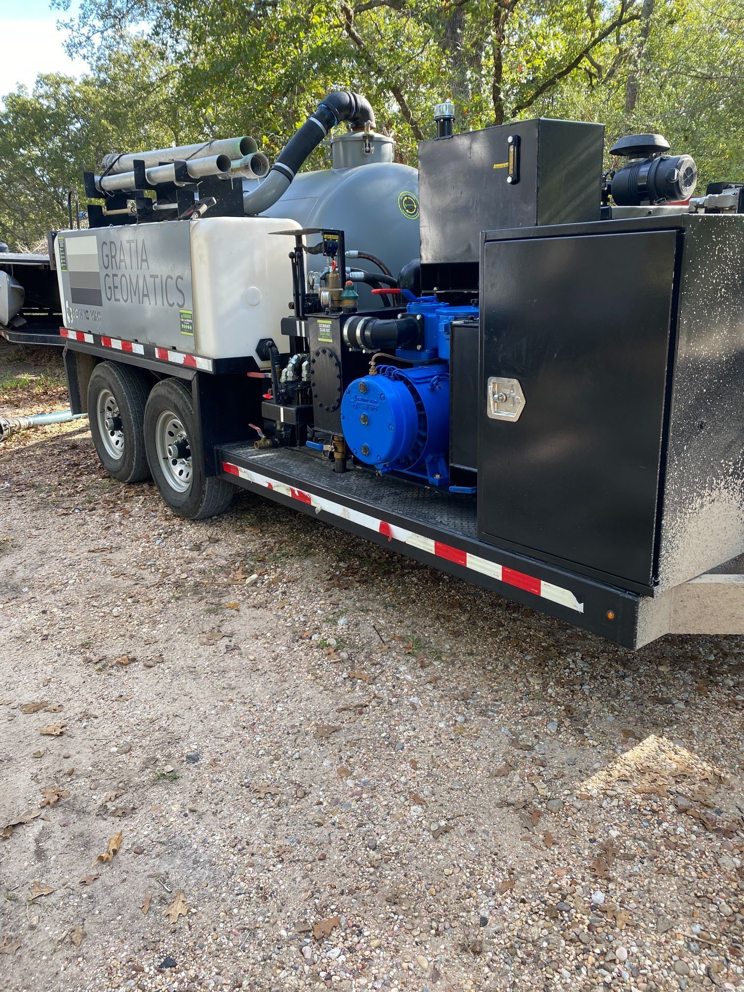 A trailer with a vacuum cleaner attached to it is parked in a gravel lot.