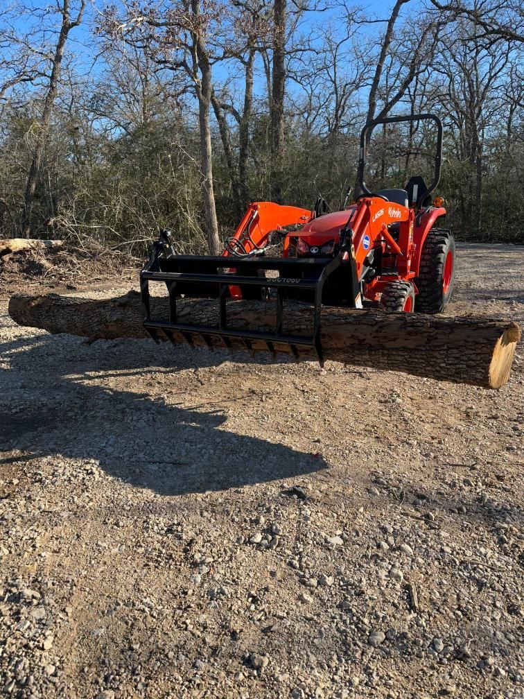A tractor is carrying a large log on a gravel road.