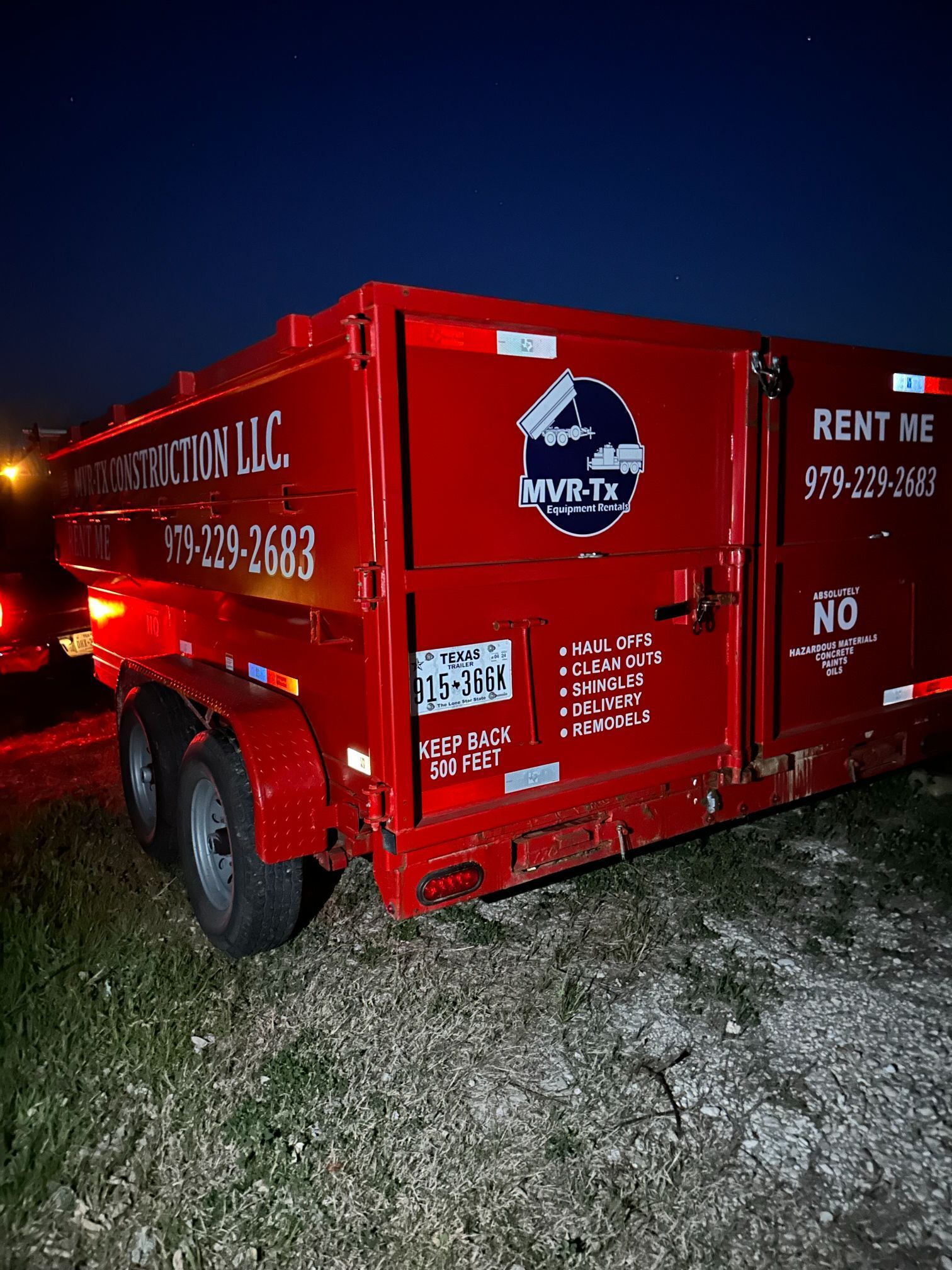 A red dumpster is parked in a field at night.