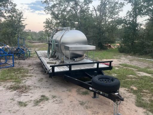 A stainless steel tank is sitting on top of a trailer in a field.