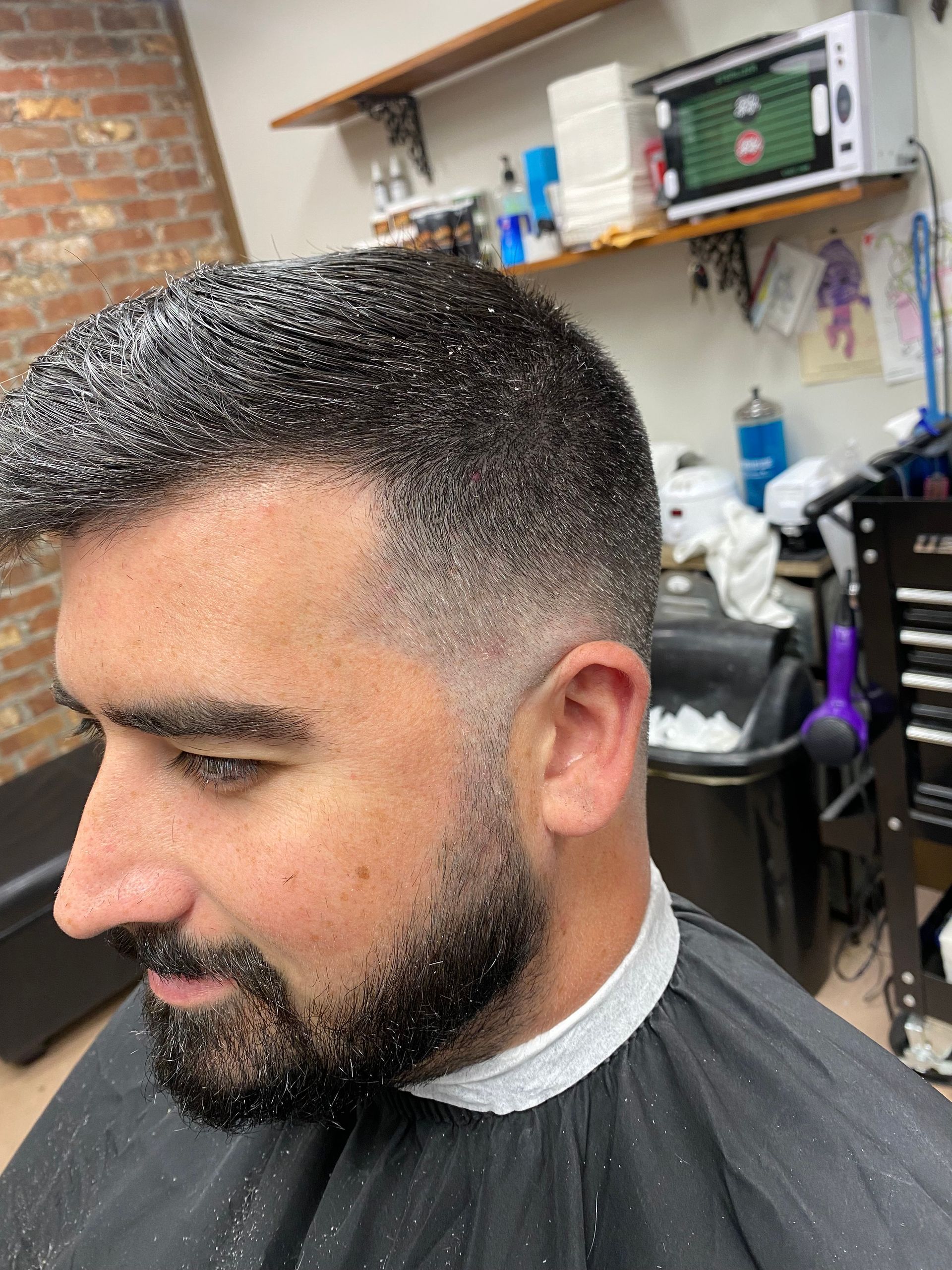 Man with a freshly cut, faded haircut, covered in hair clippings, at a barber shop.