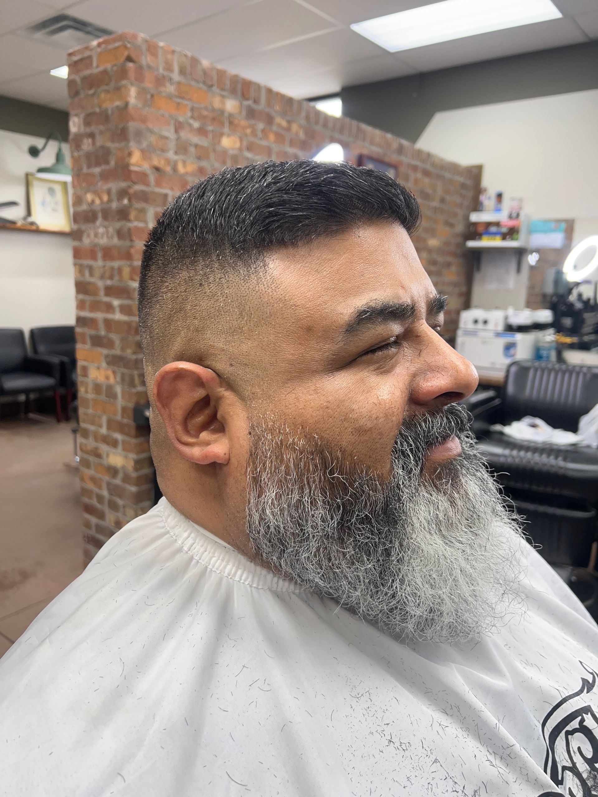 Man with a faded haircut and salt and pepper beard in a barber shop.