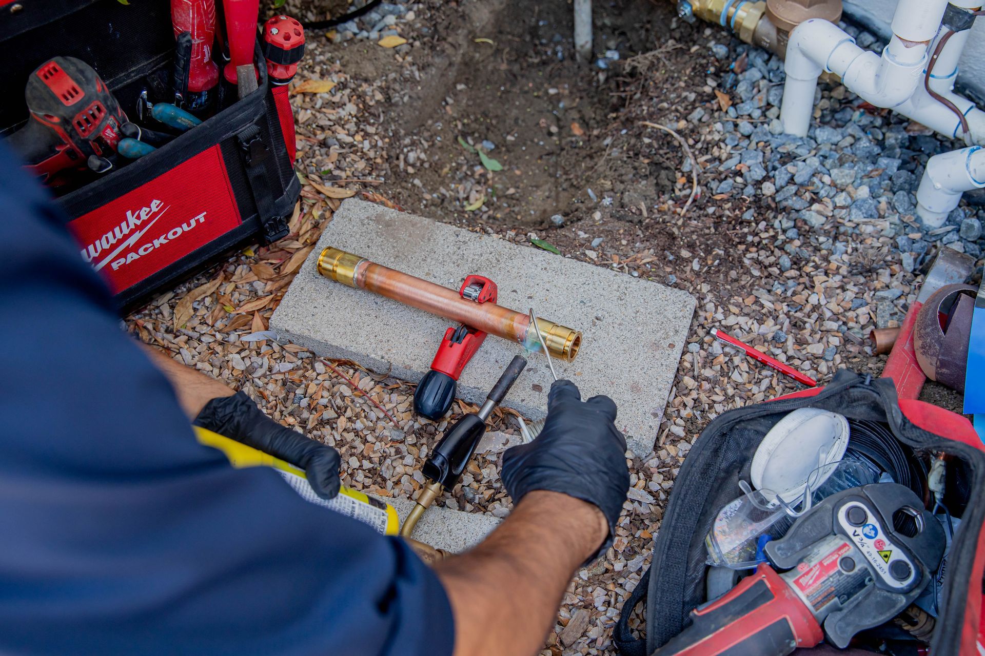 A man is working on a pipe outside with tools.