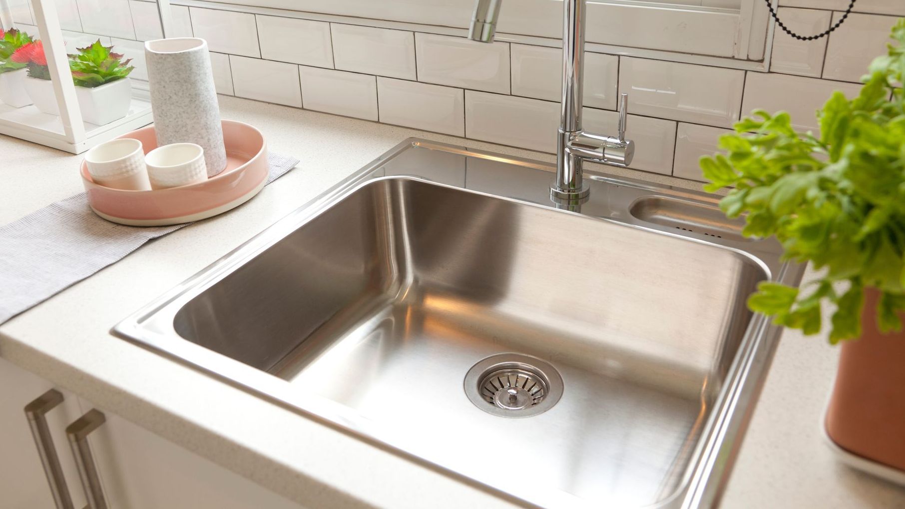 A stainless steel sink in a kitchen next to a potted plant.