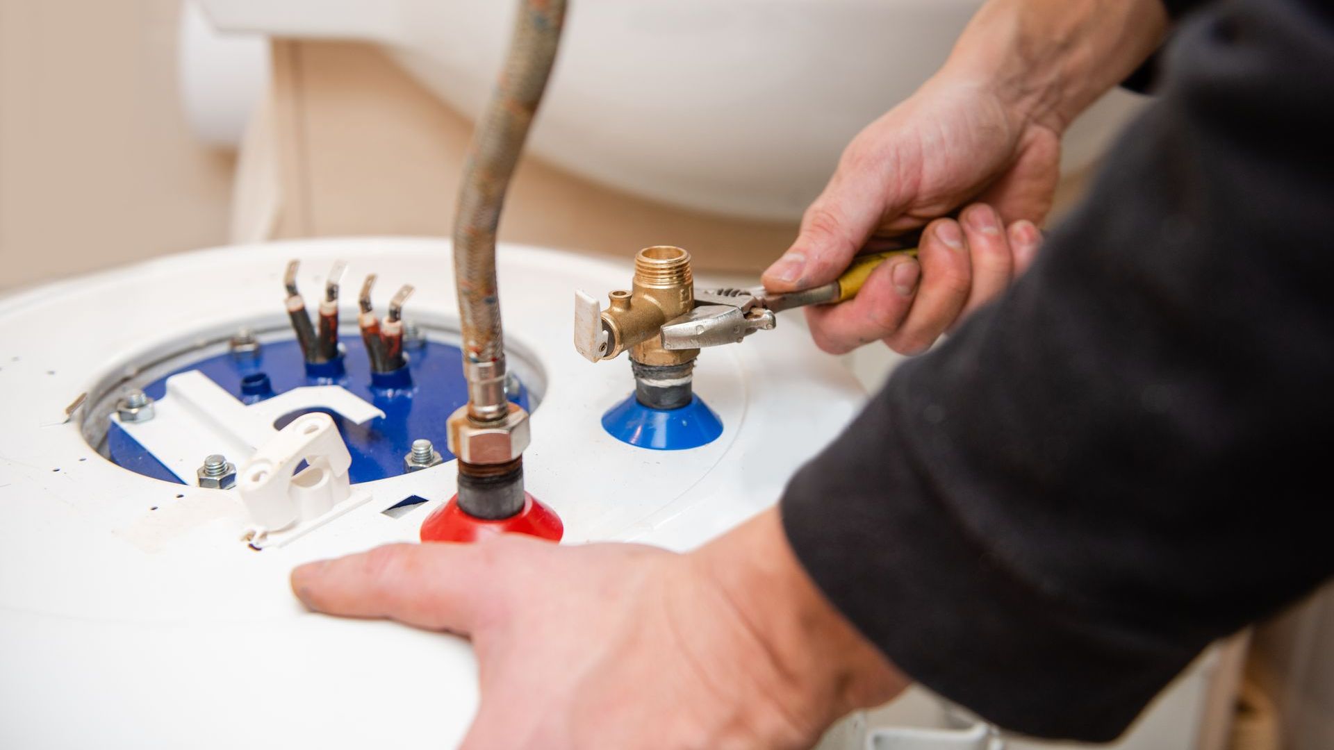 A person is fixing a water heater with a wrench.