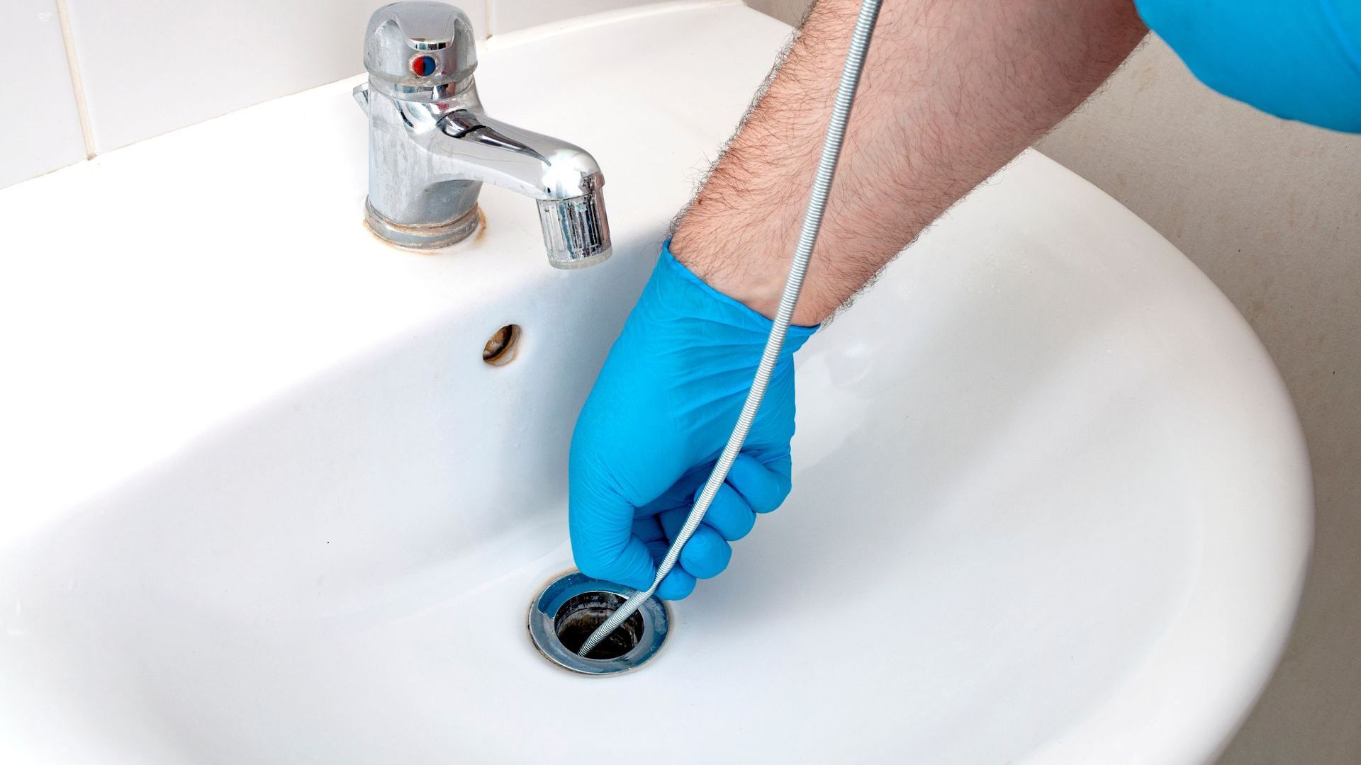 A person in blue gloves is cleaning a sink with a hose.