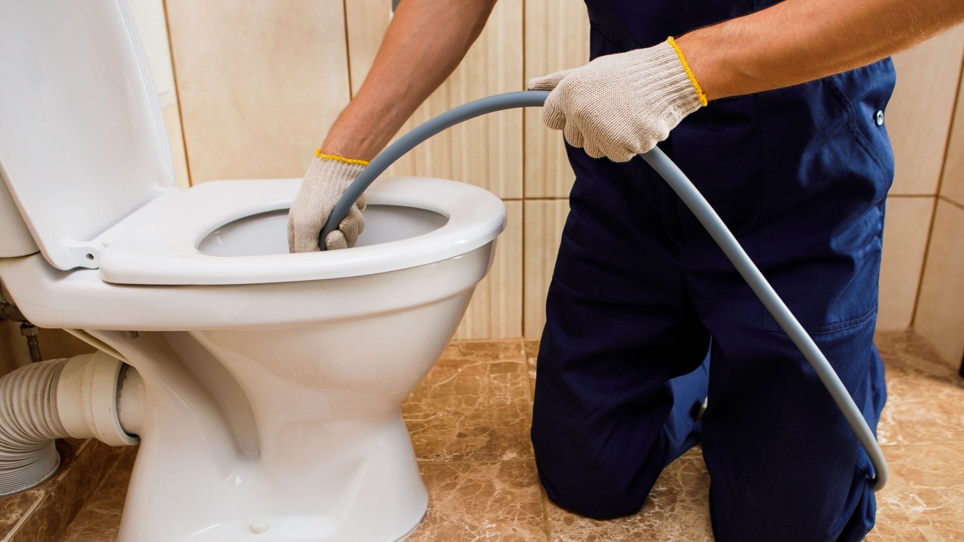 A man is kneeling down in front of a toilet with a hose.