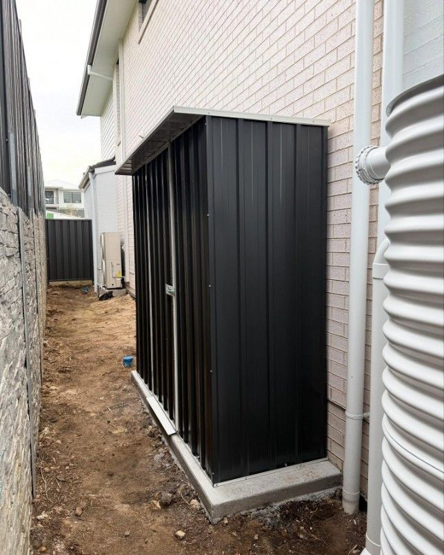 A Black Shed is Sitting on the Side of a Brick Building — JOA - Construction & Maintenance in Albion Park, NSW