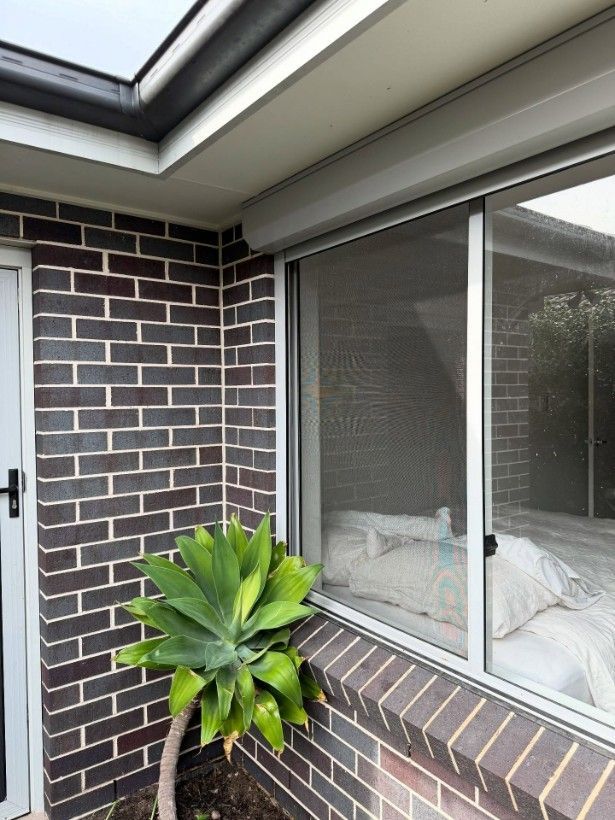 A Brick Building With a Window and a Plant in Front of It — JOA - Construction & Maintenance in Albion Park, NSW