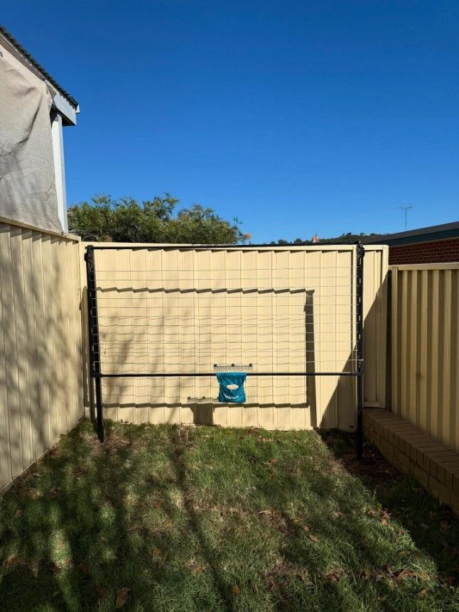 A Backyard With a Yellow Fence and a Blue Bucket in the Grass — JOA - Construction & Maintenance in Narellan, NSW