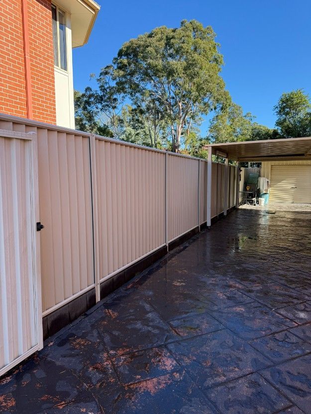 A White Fence Surrounds a Driveway in Front of a Brick House — JOA - Construction & Maintenance in Appin, NSW