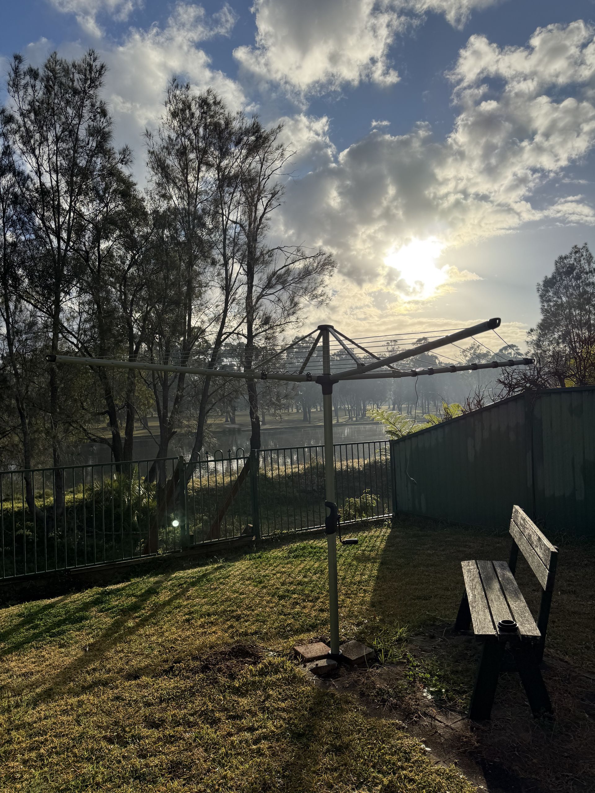 A wooden bench is sitting in the grass next to a clothes line. — JOA - Construction & Maintenance in Campbelltown, NSW