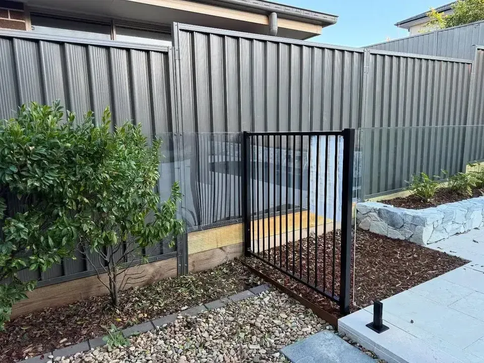A black fence with a gate in the backyard of a house. — JOA - Construction & Maintenance in Appin, NSW