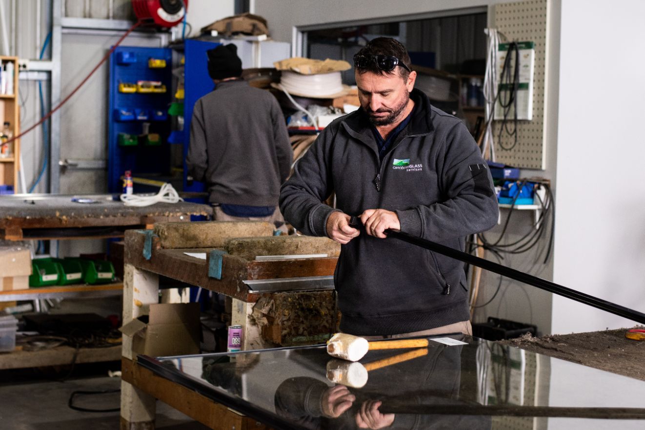 A Man is Working on a Piece of Glass in a Workshop — Canobolas Glass Service In Orange, NSW