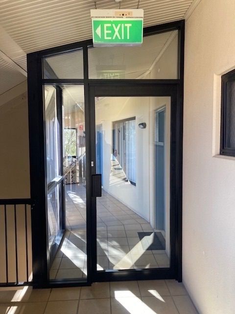 A Green Exit Sign Hangs Above a Glass Door — Canobolas Glass Service In Orange, NSW
