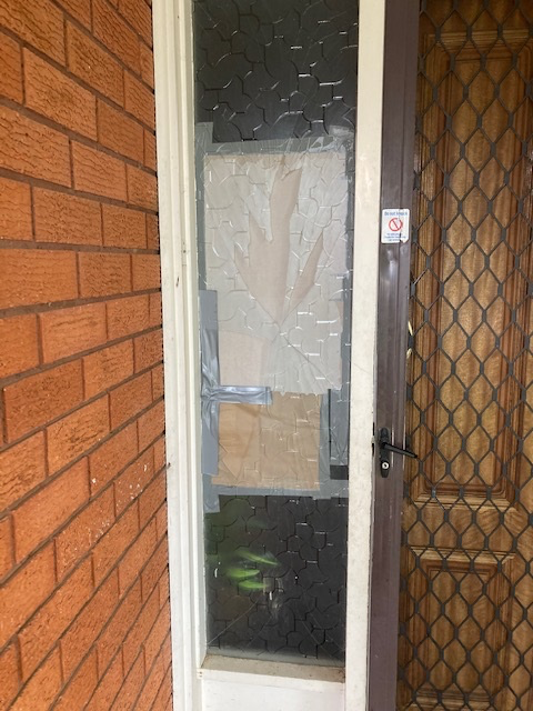 Broken glass door taped with cardboard. Brick wall and screen door visible.