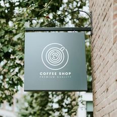 A coffee shop sign is hanging on the side of a brick building.