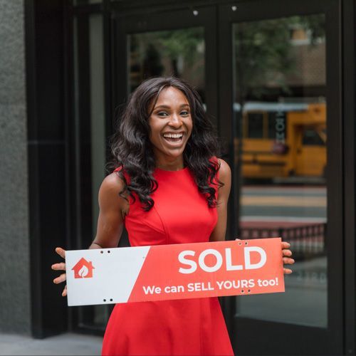 A woman in a red dress is holding a sold sign