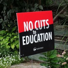 A no cuts to education sign is sitting in a garden.
