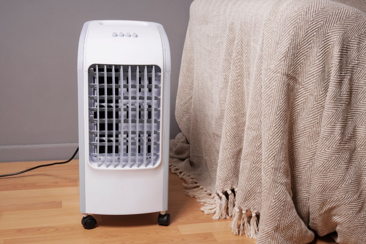 White Portable Air Cooler on Wheels by A Gray Wall, Next to A Beige Blanket — MAE Refrigeration In Portsmith, QLD