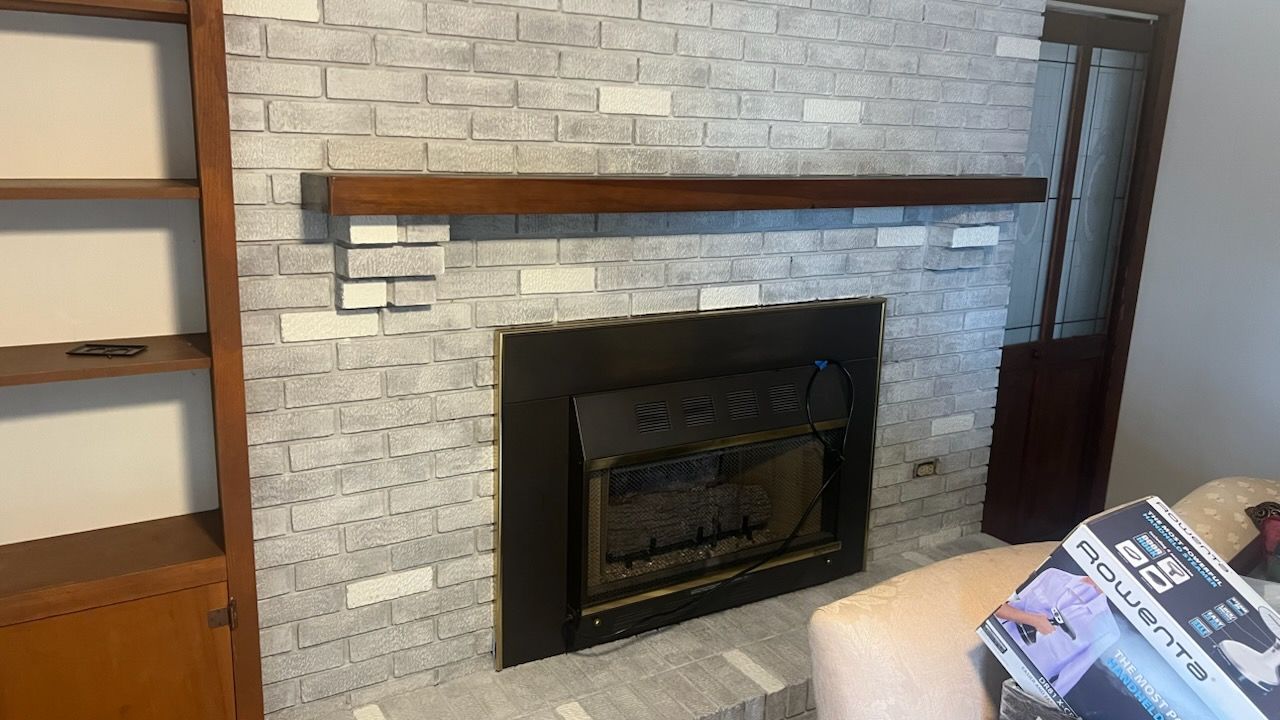 Fireplace with faux gray brick, wooden mantel, and built-in bookshelf.