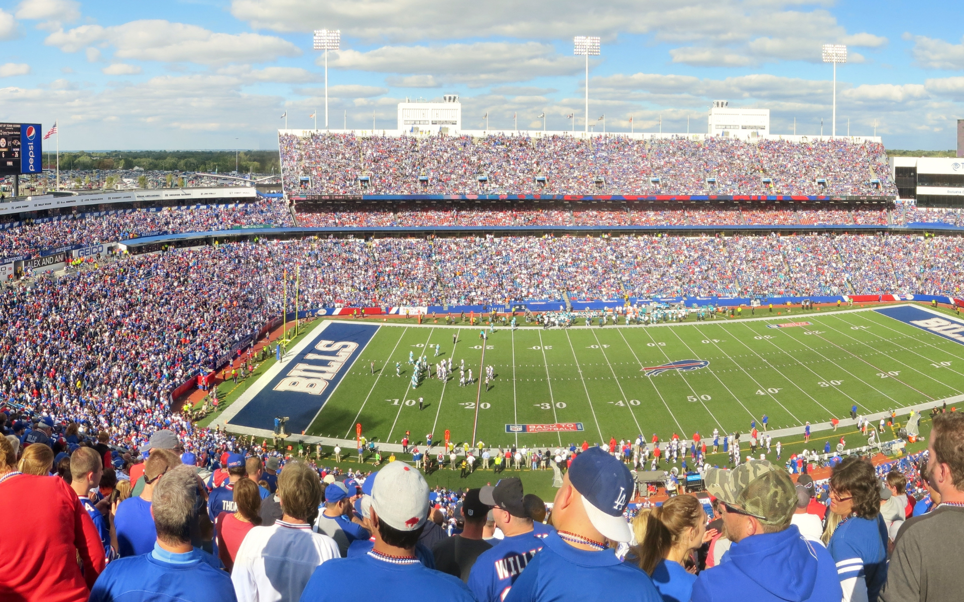 Football stadium filled with fans wearing blue. Players on the green field. 