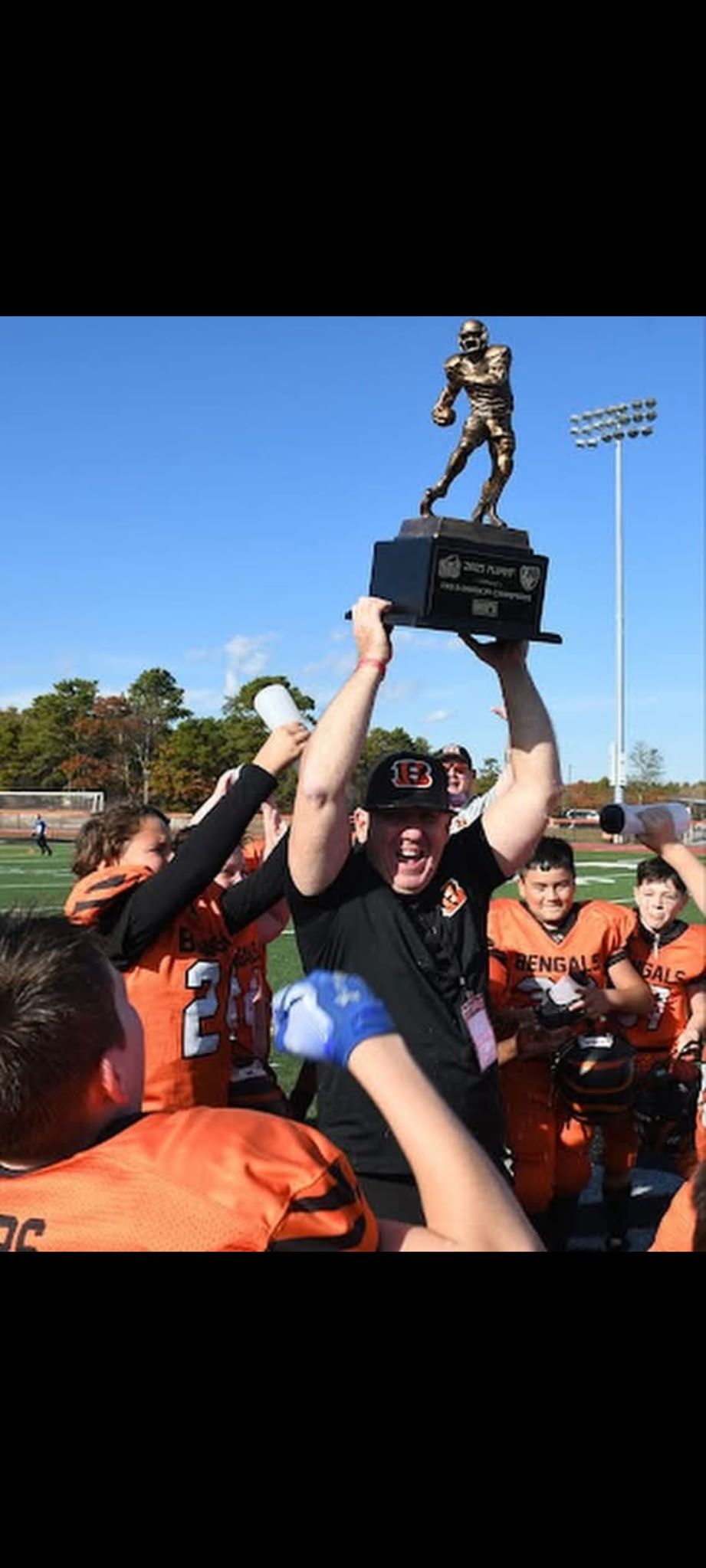 Football players in action on a grassy field; one runs with the ball, pursued by two opponents.