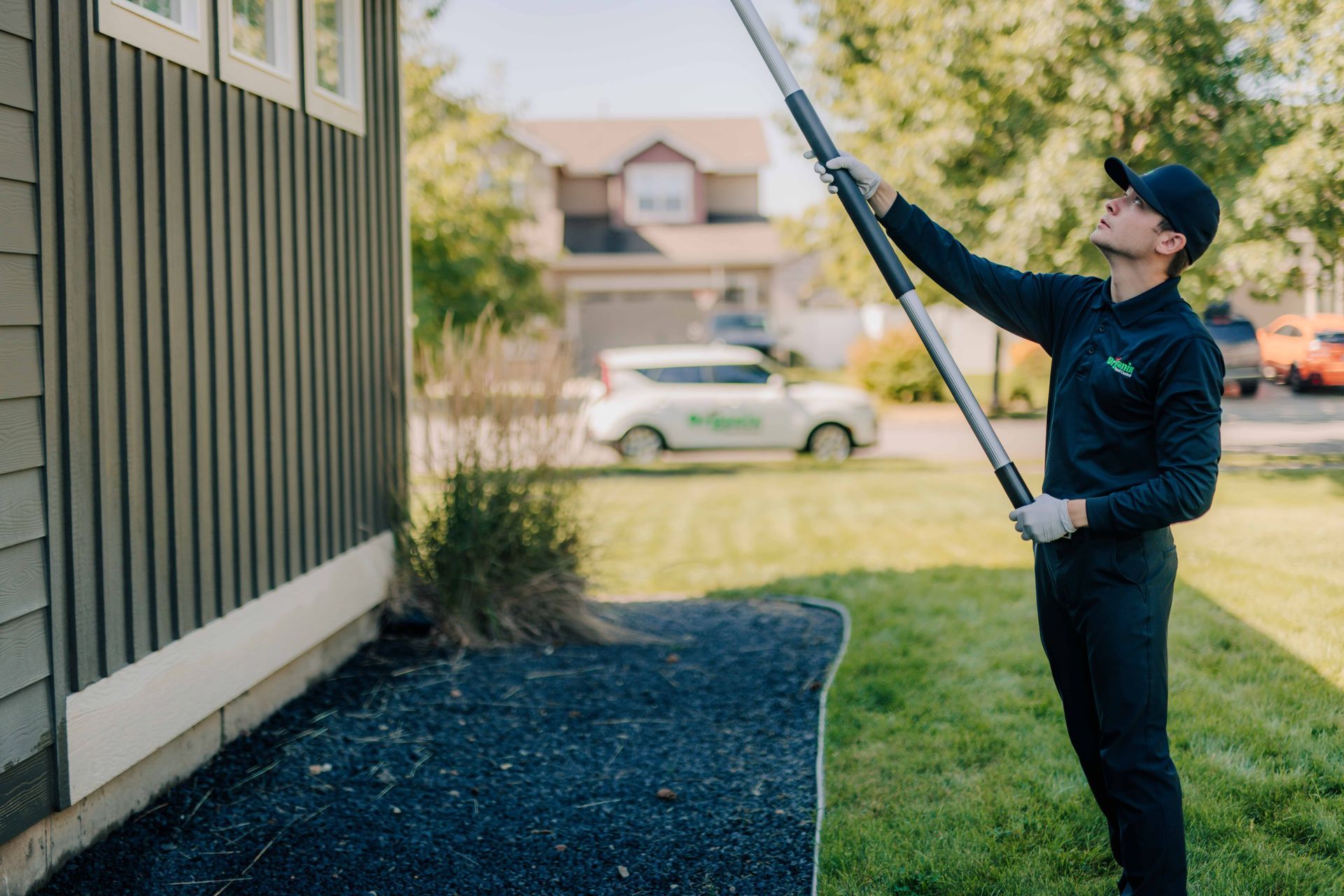 A man is standing in front of a house holding a long pole.