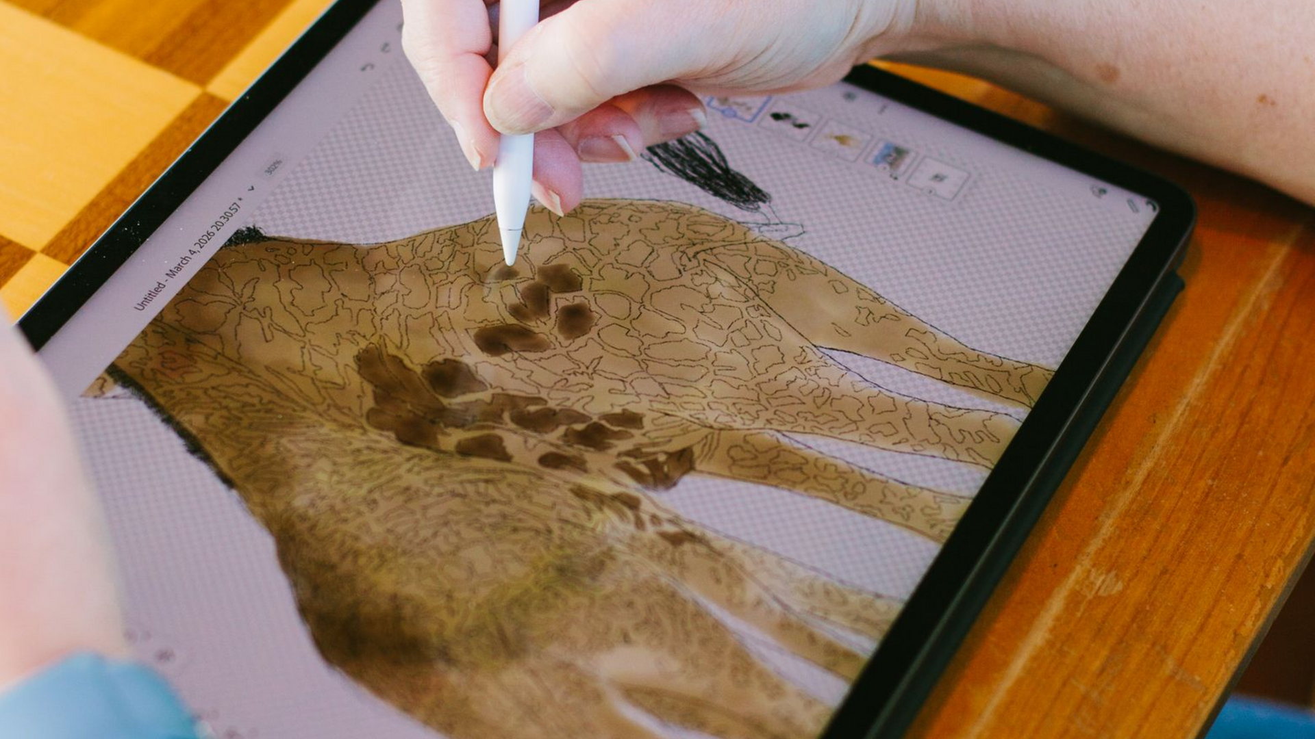 A person uses a digital stylus on a tablet screen to illustrate a giraffe's spotted pattern.