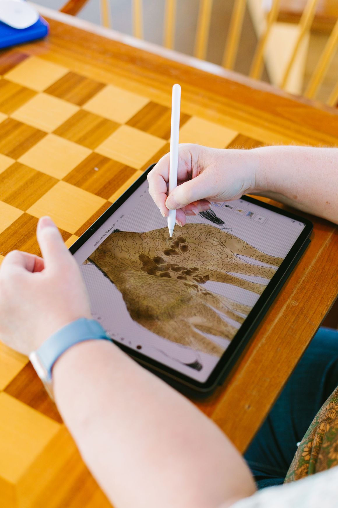 A person uses a stylus on a tablet screen showing an anatomical diagram of a hand, resting on a wooden chessboard.