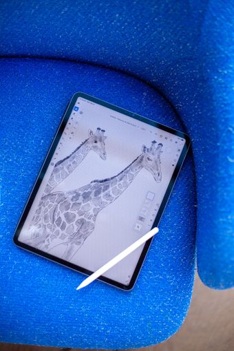 A tablet displaying a giraffe sketch, with a digital pen resting on top, set against a textured blue background.