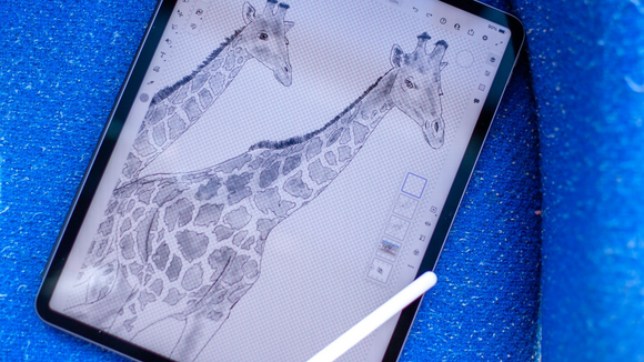 A digital drawing of two giraffes displayed on a tablet screen, positioned on a bright blue glittery surface.