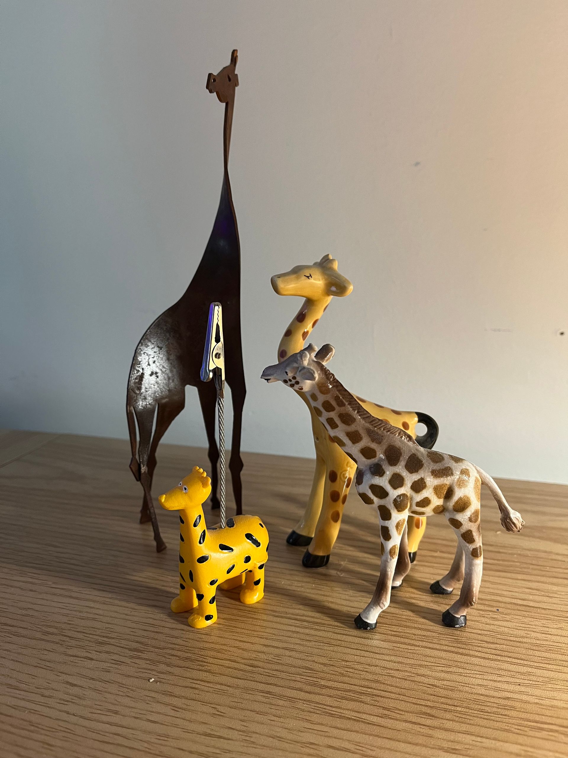 Four giraffe figurines of different styles and sizes stand on a wooden surface.