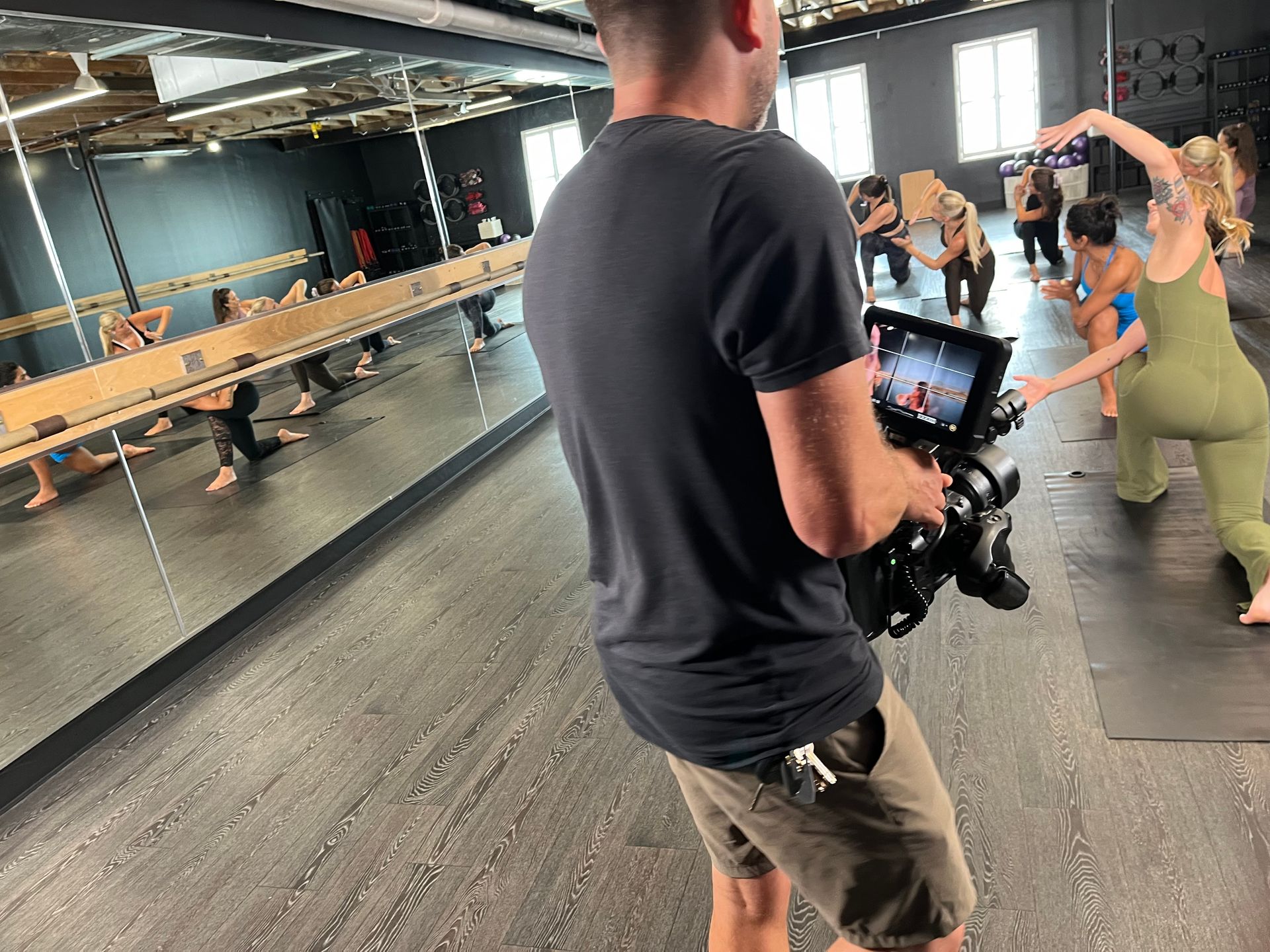 A camera operator filming a group of people doing yoga in a studio with large mirrors.