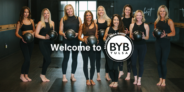 A group of nine women in black workout attire hold exercise balls in a studio with the 