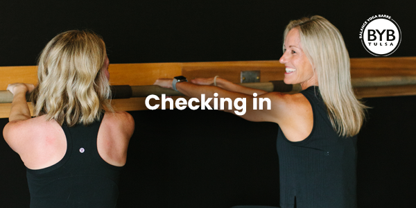 Two people in black athletic tops at a wooden barre studio with the text 