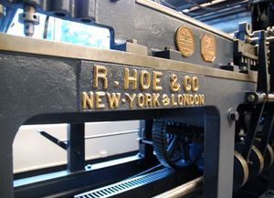 A close-up of a dark grey, industrial R. Hoe & Co. printing press with gold-painted lettering and emblems.