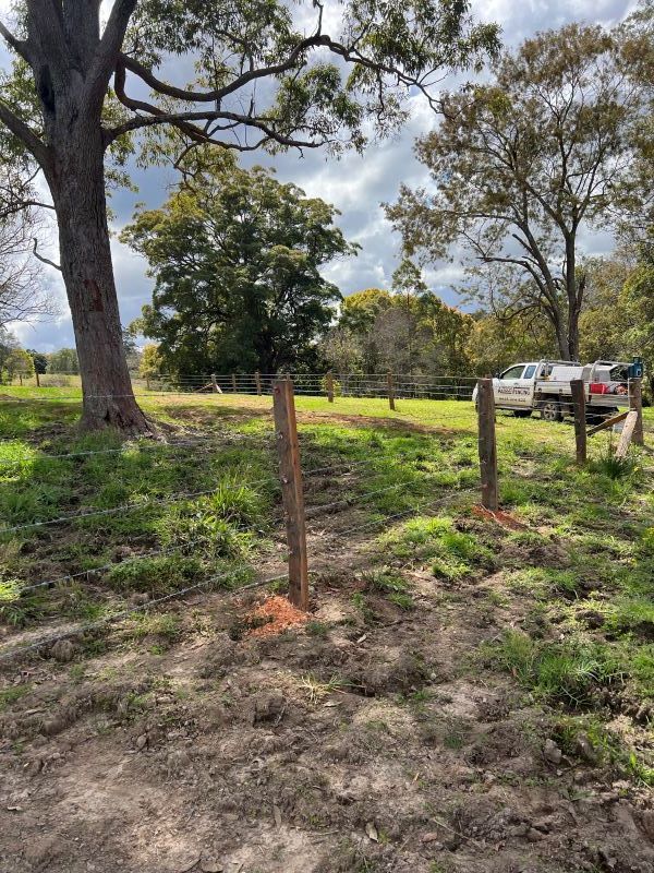 A Wooden Fence is Surrounded by Grass and Trees in a Field — Aztech Fencing In Port Macquarie, NSW