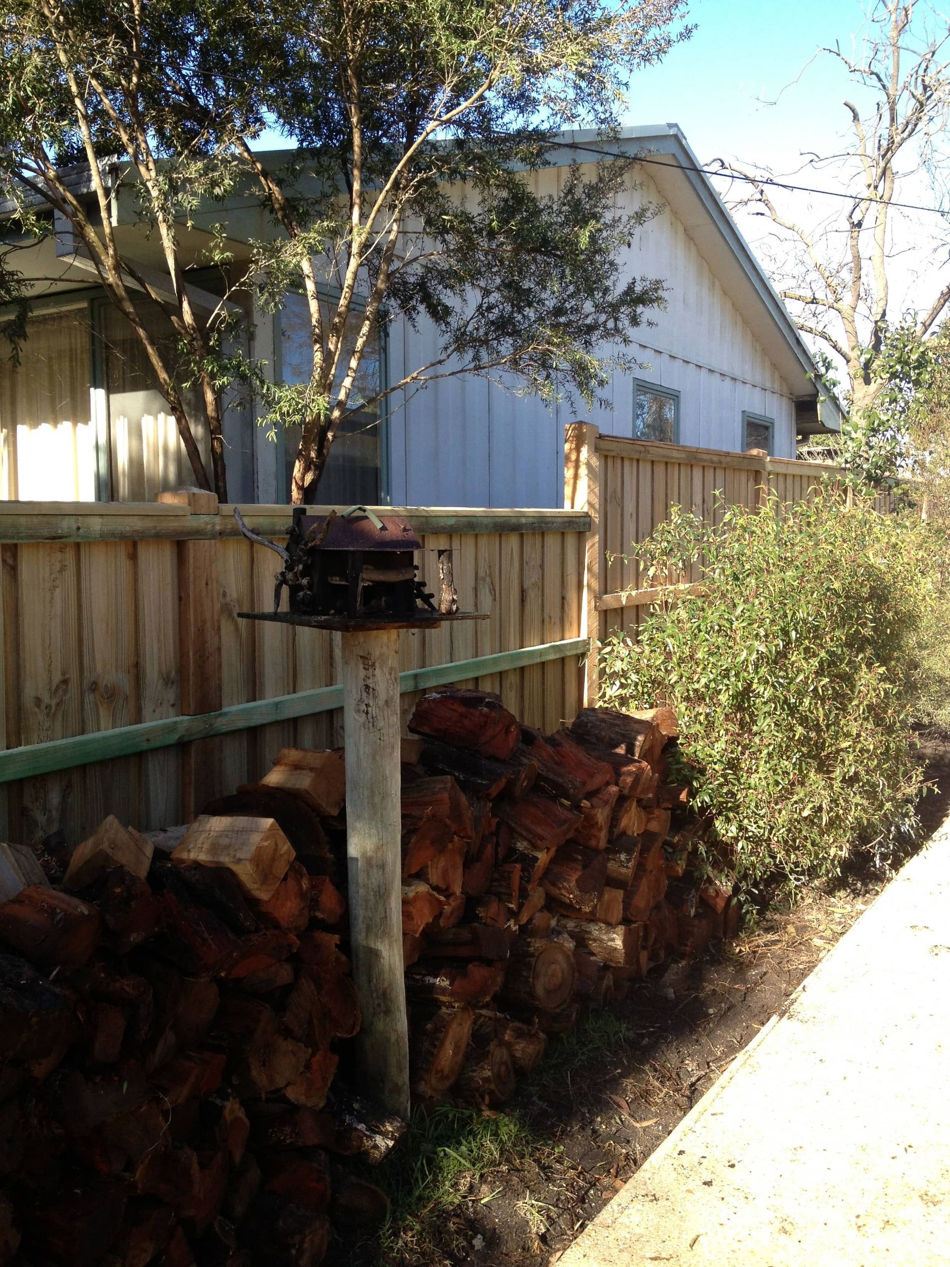 A wooden fence surrounds a pile of logs in front of a house — Aztech Fencing In Upsalls Creek, NSW