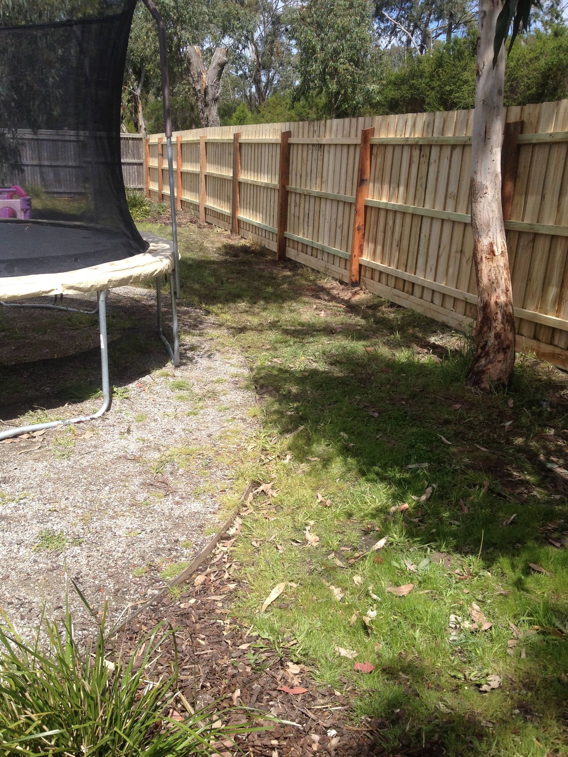 A trampoline is sitting in the grass next to a wooden fence — Aztech Fencing In Upsalls Creek, NSW