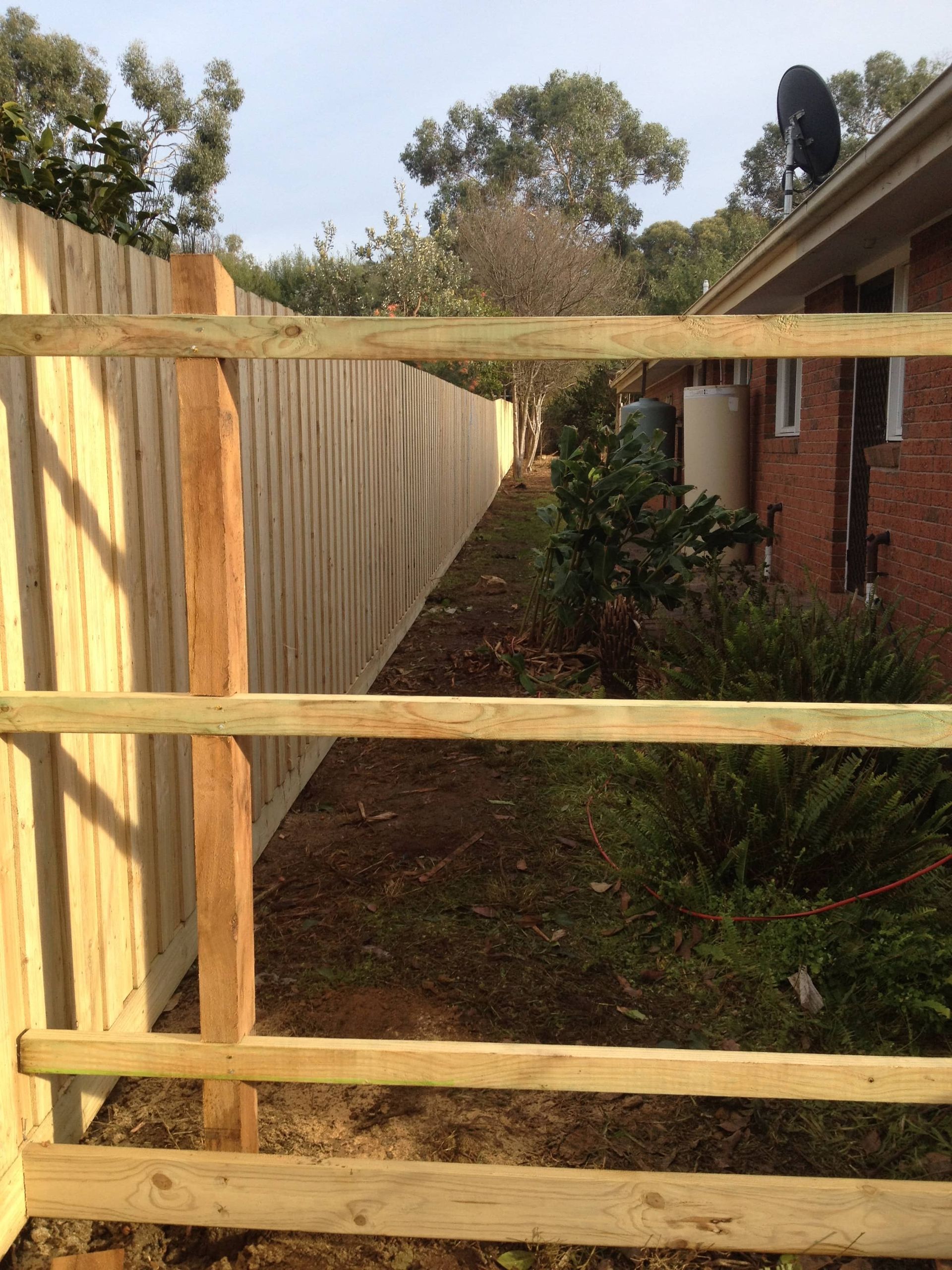 A wooden fence with a brick house in the background — Aztech Fencing In Upsalls Creek, NSW